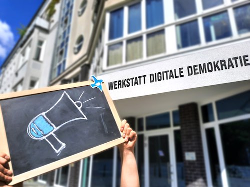 Persona sosteniendo una imagen con un micrófono, al fondo se ve el edificio de OpenPetition .